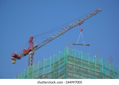 Red Tower Crane On Top Of A Construction Site, Lifting Steel Beams .