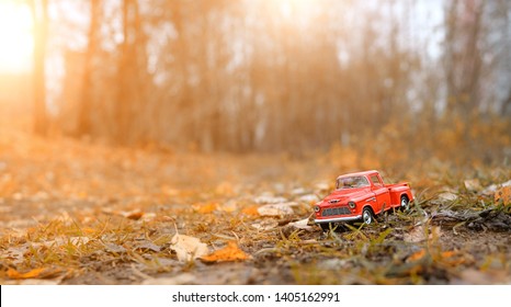 Red Toy Car In Autumn Forest. Fall  Season Concept. Beautiful Natural Landscape Background. Cute Old Retro Auto. Fall Season. Copy Space