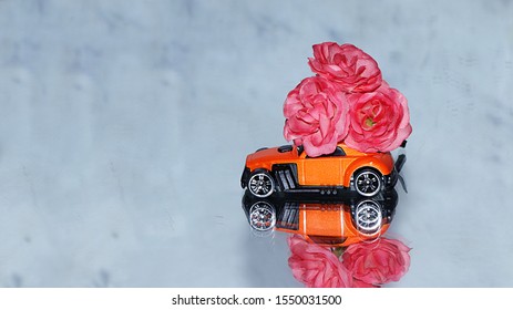 Red Toy Car With A Big Bouquet Of Flowers On A Gray Mirror Background. Congratulations On Your Birthday, Holiday, Valentine's Day, Merry Christmas, Flower Delivery For Sale, Selective Focus,