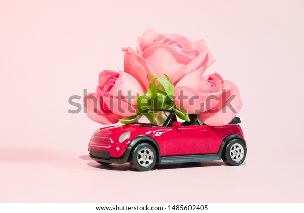 Red toy car delivering bouquet of pink rose flowers\
on pink background. February 14 card, Valentine\'s day. Flower\
delivery. 8 March, International Happy Women\'s Day St.Petersburg\
Russia 16 jul 2019
