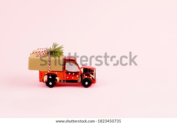 Red toy car delivering Christmas\
or New Year gift present box on pink background. Copy\
space