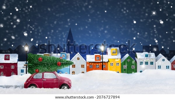 Red toy\
car delivering Christmas tree in the night snow-covered city with\
Colorful miniature houses arranged in a\
row.