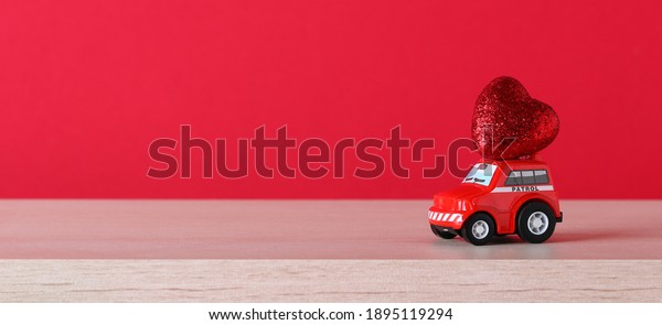 Red toy car delivering heart on red\
background. February 14 card, Valentine\'s day. Gift Delivery. 8\
March, International Happy Women\'s\
Day.