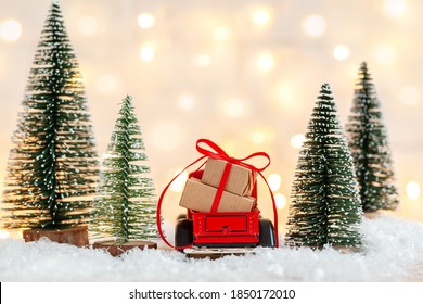 Red Toy Car Truck With Stack Of Christmas Gift Boxes Aginst Netural Background With Christmas Trees. Holiday Greeting Card. Back View.