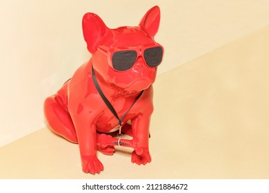 Red toy guard dog sitting on its hind legs with black glasses and a hidden surveillance camera on its forehead on a beige wall background. ?opy space.
