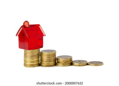 A red toy house stands at the top of a staircase made from stacks of yellow gold coins, isolated on white, side view. The concept of reducing the profitability of the real estate and mortgage market