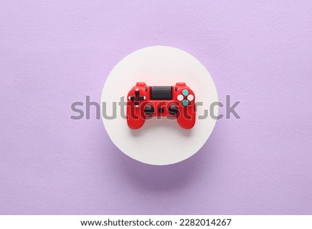 Red toy miniature gamepad on a purple background with white circle. Top view