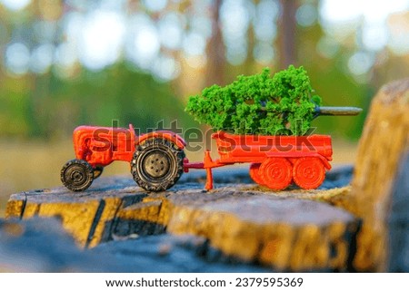 Red toy tractor with a tiny green sapling in its bed is placed on a tree stump in the forest. Deforestation issue related concept.