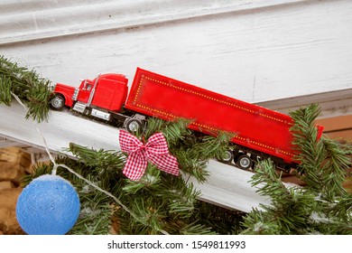 Red Toy Truck And New Year Decorations On The Street. A Truck That Brings Gifts. A Car Rides Past A Christmas Tree On A Wooden Ramp. Concept.