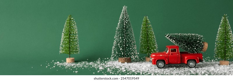 A red toy truck transports a snow-covered Christmas tree through a festive winter landscape with miniature trees. Ideal for holiday themes and winter celebrations - Powered by Shutterstock