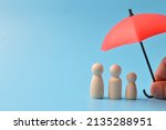 Red toy umbrella and wooden doll figures isolated on a blue background. Insurance coverage concept.