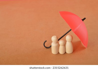 Red toy umbrella and wooden doll figures isolated on a brown background. Insurance coverage concept. - Shutterstock ID 2315262631