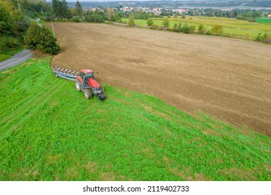 A red tractor plows the land sown with green manure in the field, near the railway and the paved road. Agricultural industry. View from above. - Shutterstock ID 2119402733