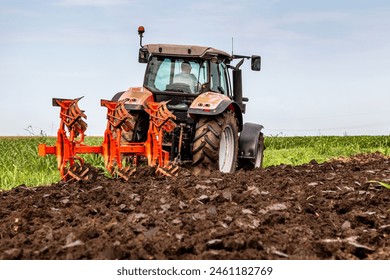 Red tractor plows through fertile soil with a vibrant green landscape in the background