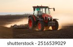 A red tractor prepares the land with a plow. Preparing land for a new crop plantation during sunset

