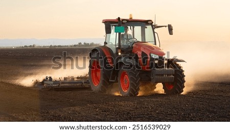 A red tractor prepares the land with a plow. Preparing land for a new crop plantation during sunset

