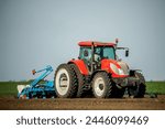 Red tractor at seeding in a vast, freshly plowed agricultural field under a clear sky