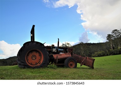 A Red Tractor Sits Forgotten In A Lush, Green Paddock Surrounded By Australia Bush Landscape, Topped With A Bright Blue Sky And Thick White Clouds