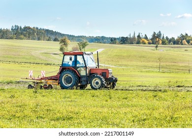 Red tractor turning cut grass to dry for hay in Czech Republic. Agricultural works at farmlands. Autumn day on the farm. - Shutterstock ID 2217001149