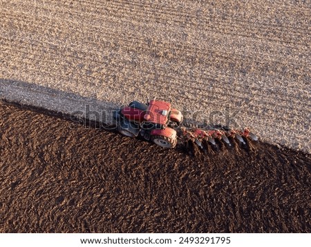 Red tractor working in the field on sunrise. Plowing field in early spring with tractor, concept of agriculture and farming