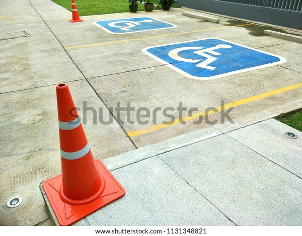 Red traffic cones and sign of\
wheelchair on the ground in hospital parking area, select focus\
