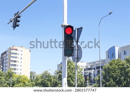 Red traffic light at city intersection on sunny day. Urban transportation infrastructure and road safety concept. Street signal controlling vehicle movement. Modern city background.