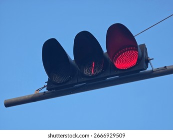 Red traffic light and countdown timer seen hanging on pole in blue sky background, possibly in urban street intersection.
