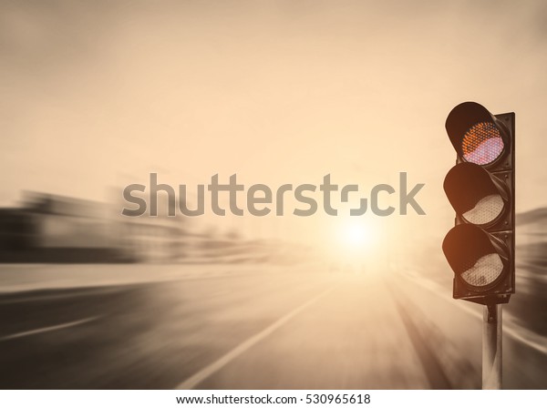 Red traffic light on the expressway asphalt road\
with car in a city landscape at sunrise. light sign for car stop\
and speed reduction. Dangerous,warning signal,semaphore. Driving on\
a Highway.