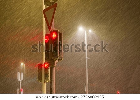 Red traffic light shining through dense snowfall on a winter night representing stop danger low visibility and increased accident risk during extreme winter weather