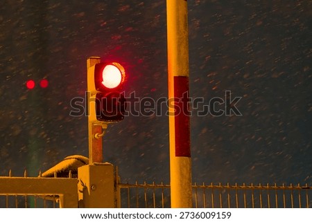 Red traffic light shining through dense snowfall on a winter night representing stop danger low visibility and increased accident risk during extreme winter weather