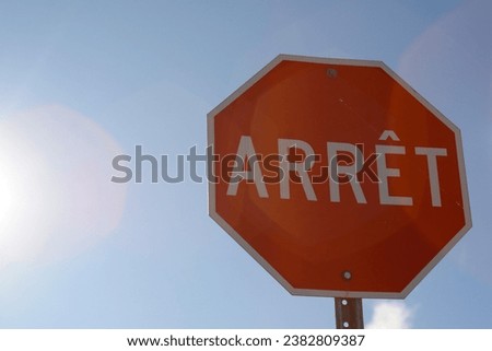 A red traffic sign on a blue sky background with sun rays. French Canadian sign for Stop.