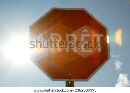 A red traffic sign on a blue sky background with sun rays. French Canadian sign for Stop.