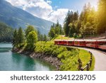 Red train moving along lake in beautiful mountain landscape in Switzerland
