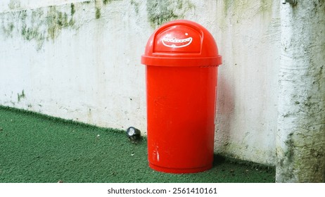 A red trash can with a smiling face on it. The trash can is sitting on a grassy area