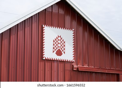 A Red Tree Of Life Pattern Quilt Hanging On The Front Of A Barn With Red Metal Siding.   