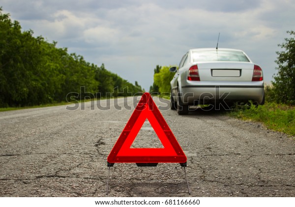 Red triangle of a car on the road. Car warning\
triangle on the road against the city in the evening. Breakdown of\
the car in bad weather.