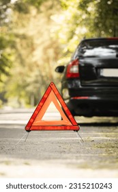 Red triangle, red emergency stop sign and black car with technical problems in the blurred background. Emergency stop of the car on the road. Safety procedure while having a vehicle broken down - Shutterstock ID 2315210243