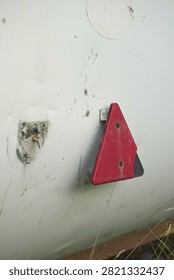 Red triangle reflector on a damaged white trailer panel with exposed wire