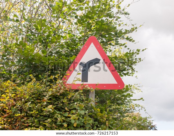 red triangle warning bend in road up ahead sign pole\
metal leaves sky