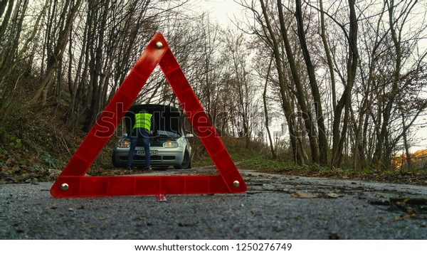 Red triangle warning sign\
closeup, man trying to find out a problem on car engine. Selective\
focus