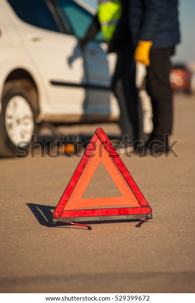 Red\
triangle warning sign on the background of car technician and\
driver checking auto. Fall or winter sunny\
day.