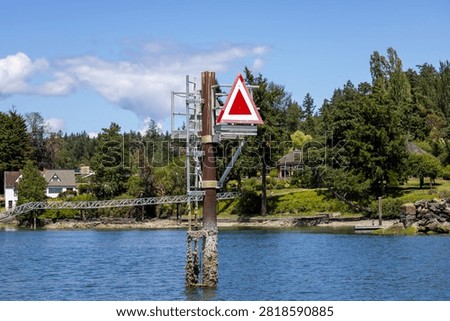 Red triangular channel marker on a navigation post over water by waterfront homes in Sidney, Vancouver Island, BC, Canada