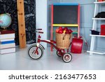 Red tricycle with basket apples. Back to school. Elementary school. Chalkboard, Books, globe in classroom. Teachers Day. Empty classroom with blackboard. Kindergarten. Interior of children