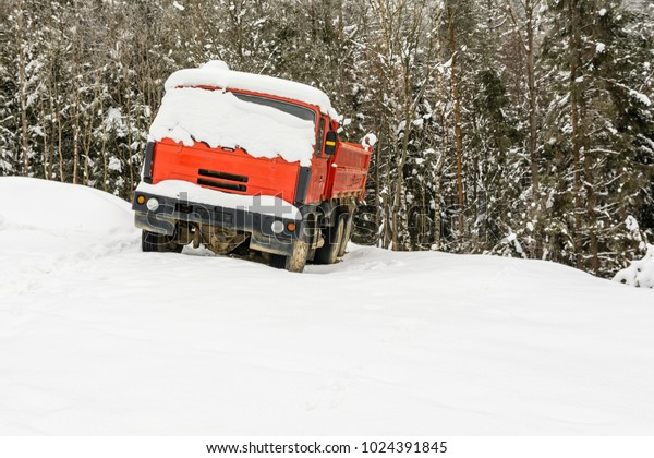 A\
red truck covered with snow is standing by the\
forest