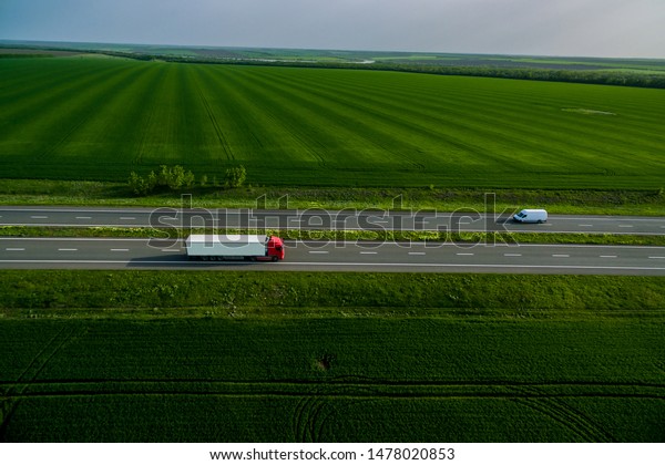red truck driving on asphalt road along the\
green fields. seen from the air. Aerial view landscape. drone\
photography.  cargo\
delivery
