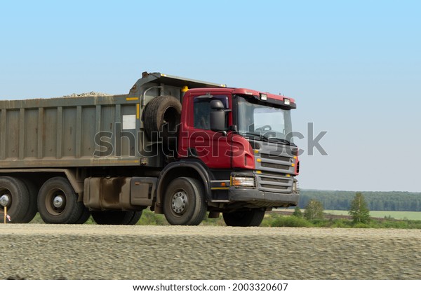 The red truck is driving on a dirt road. A\
truck carries rubble in the\
countryside.
