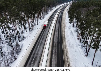 Red Truck On The Higthway. Cargo Driving By Road Seen From The Air. Top View Landscape. Shooting From A Drone. Cargo Delivery In Winter. Aerial View Of Snow Covered Road In Winter Forest 