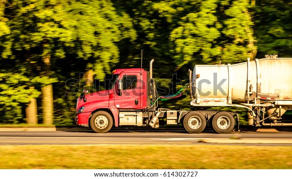 A red truck is\
running down the highway captured early morning during summer\
season. This image was captured using panning technique to blur the\
background and emphasize\
motion.