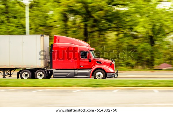 A red truck is\
running down the highway captured early morning during summer\
season. This image was captured using panning technique to blur the\
background and emphasize\
motion.