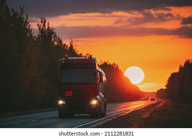 Red Truck Or Tractor Unit, Prime Mover, Traction Unit In Motion On Road, Freeway. Asphalt Motorway Highway Against Background Of Big Sunset Sun. Business Transportation And Trucking Industry Red Truck